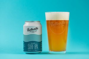 How to drink beer like a pro? Photograph of a blue can of Belleville Brewery Surf IPA with a pint glass of golden beer next to it.