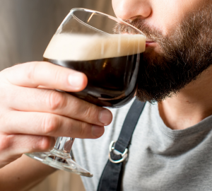 How to drink beer like a pro? Photograph of a bearded man taking a sip of a goblet glass filled with dark beer