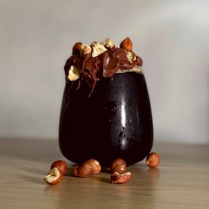 Introducing Nutshella Milk Stout. A photograph of a curved goblet glass of Nutshella Milk Stout, with molten chocolate and hazelnuts overflowing from the glass and a dark black beer within.