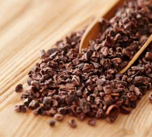 Introducing Nutshella Milk Stout. Photograph of cocoa nibs in a wooden scoop on a wooden table